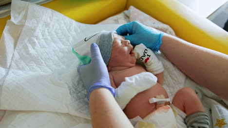 caring nurse's hands in gloves dressing the baby. newborn child in cap, mittens, socks and diaper. top view.