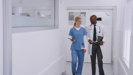 médico en bata blanca y enfermera en scrubs teniendo una discusión sobre la tableta digital en el pasillo del hospital