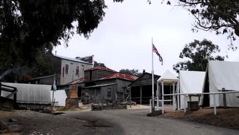 a scene featuring rustic buildings, a flagpole, and a dirt path under a cloudy sky.