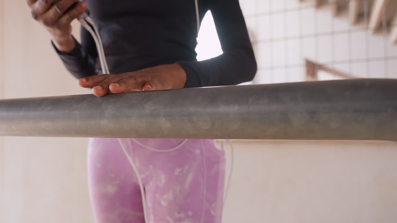 black woman dancer at barre practicing warmup in pink leggings and black top, steady hands on metal rail, soft natural light, poised posture and concentrated breathing during studio rehearsal