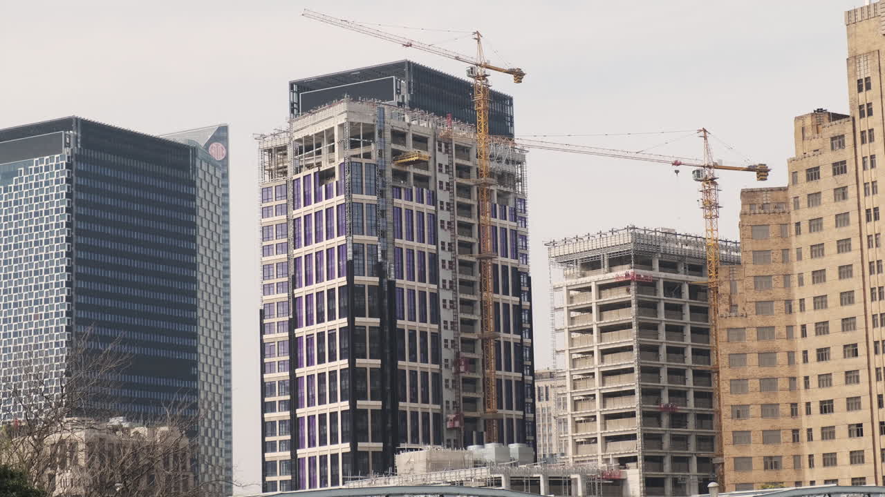 Rapido sviluppo urbano di Shanghai, moderni grattacieli in costruzione con diverse grandi gru industriali gialle attive sullo sfondo di un cielo velato