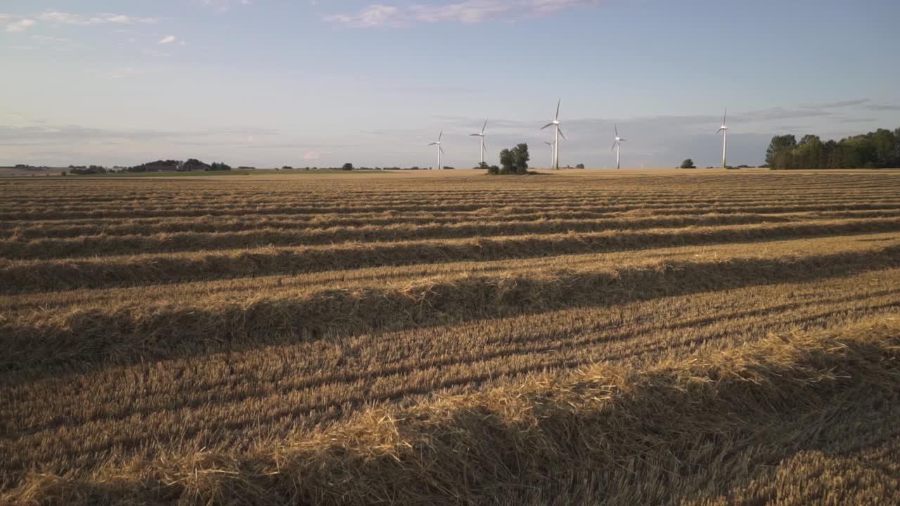 panning over a harvested field of wheat. in the horizon there are wind mills and you can see turbines spinning
