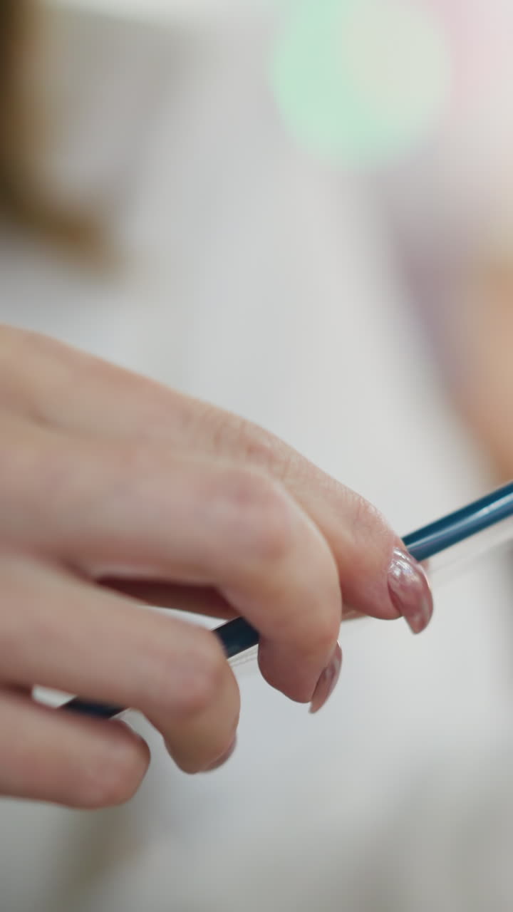 primer plano de manos con uñas pintadas sosteniendo delicadamente una paja y observándola con enfoque en un entorno interior, luces bokeh de colores borrosos en el fondo