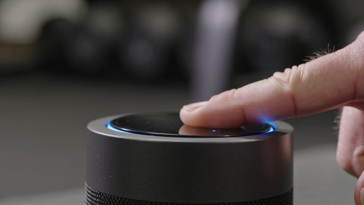 Toccando con l'indice destro per attivare lo smart speaker sulla scrivania, che mostra la parte superiore lucida e touch e un anello LED blu.