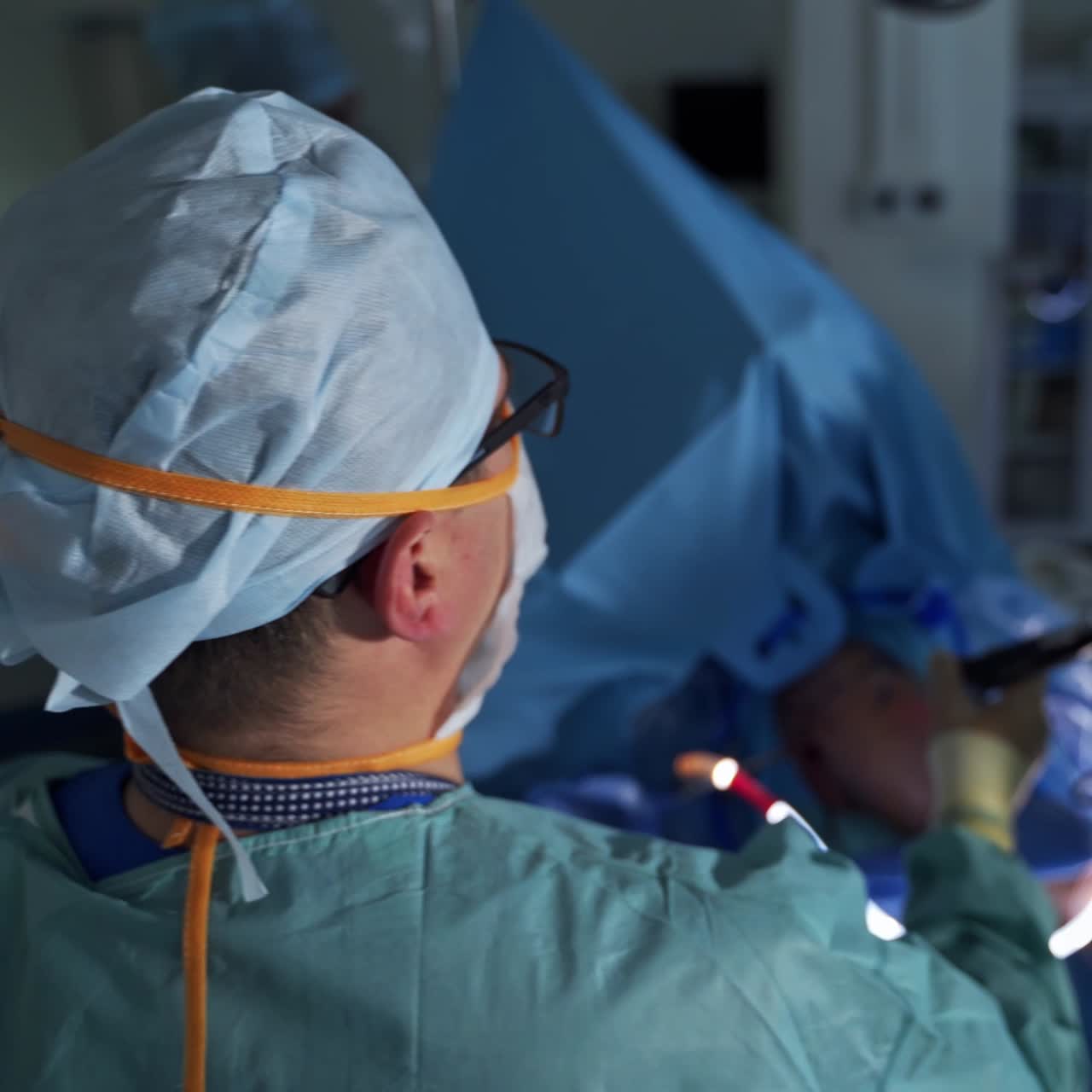 Overlæge holder og bevæger udstyr indført i patientens krop. Medicinsk team står omkring patienten. Sløret baggrund
