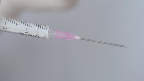 hand with disposable glove removing plastic cap of syringe needle - close up