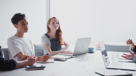 Equipo-De-Jóvenes-Empresarias-Con-Computadoras-Portátiles-Y-Tabletas-Reunidas-Alrededor-De-Una-Mesa-En-Un-Espacio-De-Trabajo-Moderno