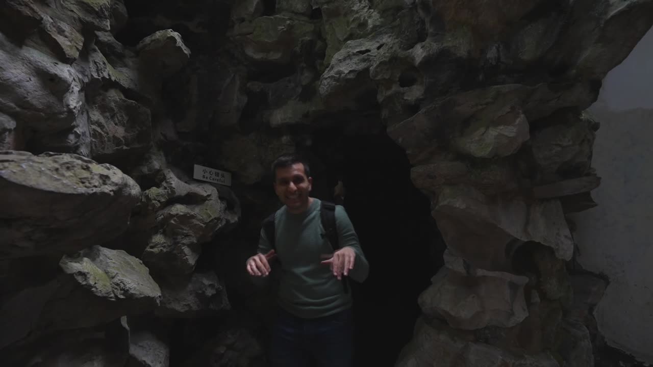 Slow motion of a tourist emerging from a Yuyuan Garden cave smiling and gesturing. Shangha, China