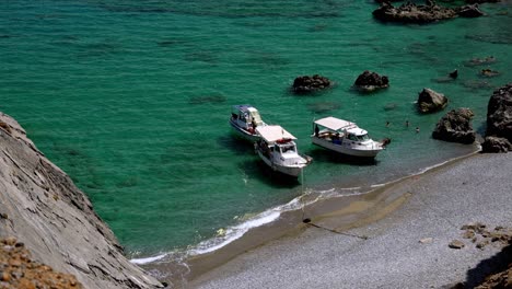 three small boats with people moored at a deserted exotic beach , people swimming