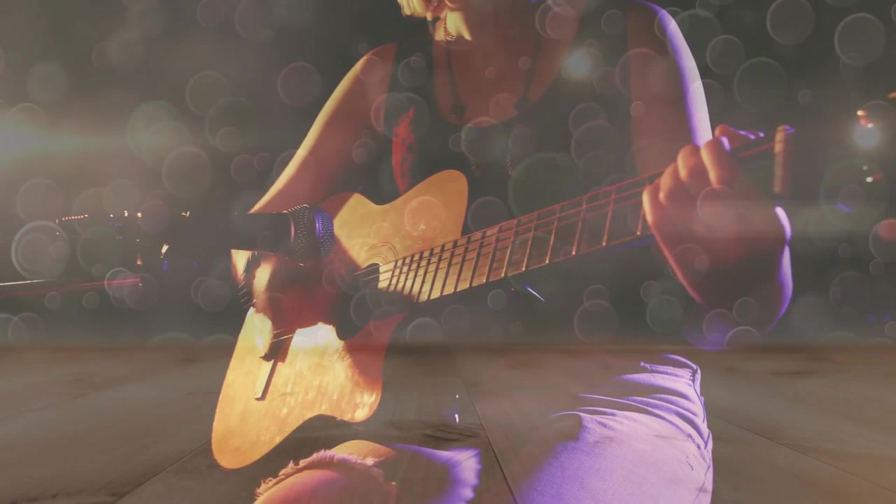 Chitarrista adolescente che porta una chitarra acustica nell'inquadratura, esegue un brano sotto i caldi bagliori di un riflettore.