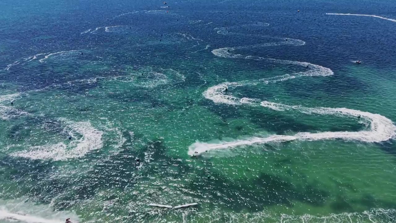Jetski riders create patterns in ocean water during sunny day