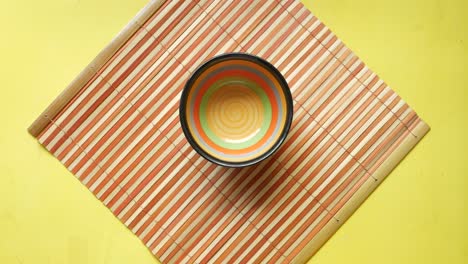 hand holding a lemon in a bowl on a bamboo placemat