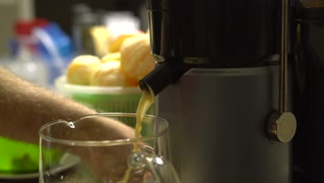 close up of person using electric juicer with nozzle pouring healthy fruit juice into glass pitcher - white caucasian male adding fruits into juicer making healthy fresh fruit juice selective focus