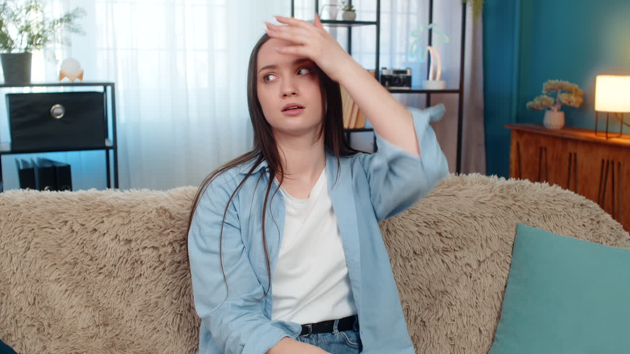 Young woman on sofa upset disappointed doing facepalm gesture frustrated unhappy with mistake