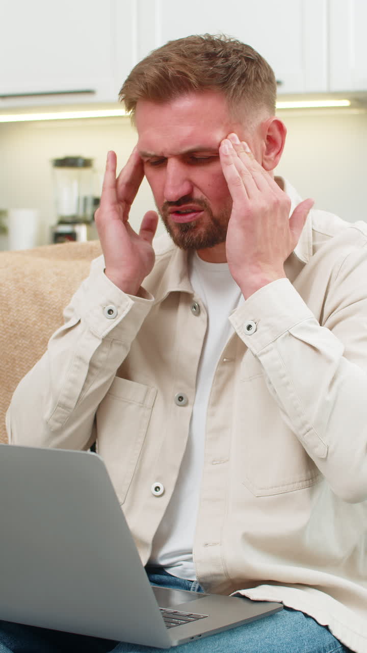 Young man with laptop suffers headache rubs temples closes eyes takes breath long break relief calm
