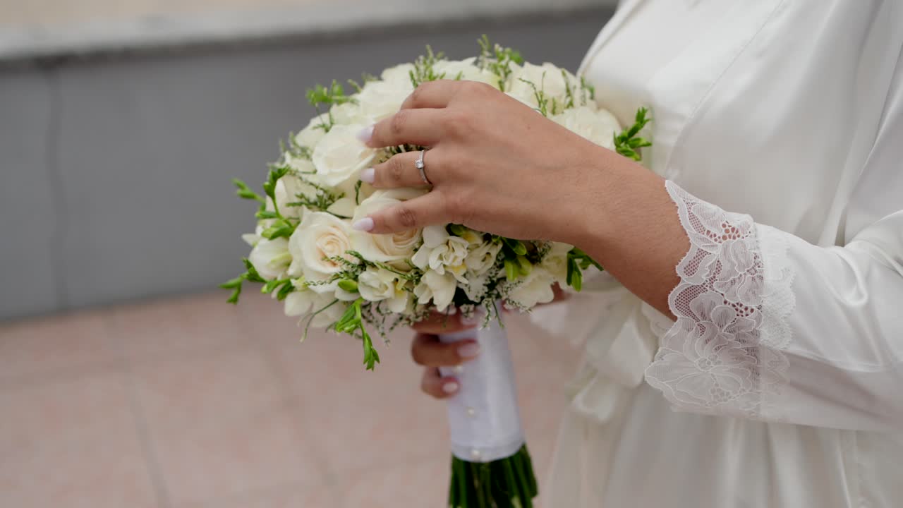 Sposa in vestaglia di pizzo che sistema un bouquet di rose bianche e verde all'aperto