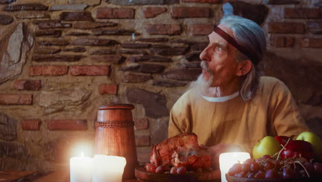 old lord looks at flying snow at dining table. mature aristocrat smiles to coming guest during rich banquet in pub. elderly nobleman in winter inn at snowstorm