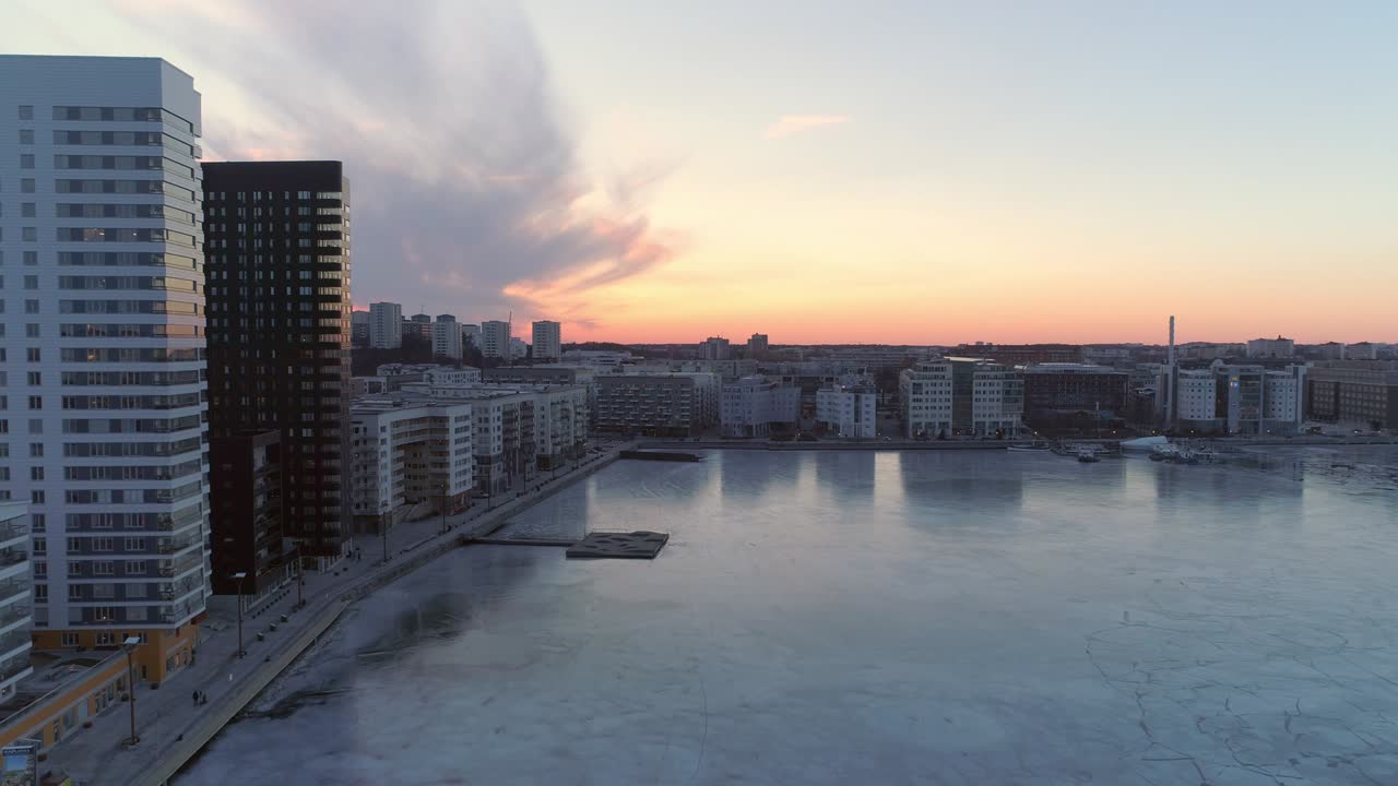 Aerial view of modern office buildings next to frozen bay in Stockholm, Sweden. Drone shot flying next to contemporary residential district at sunset