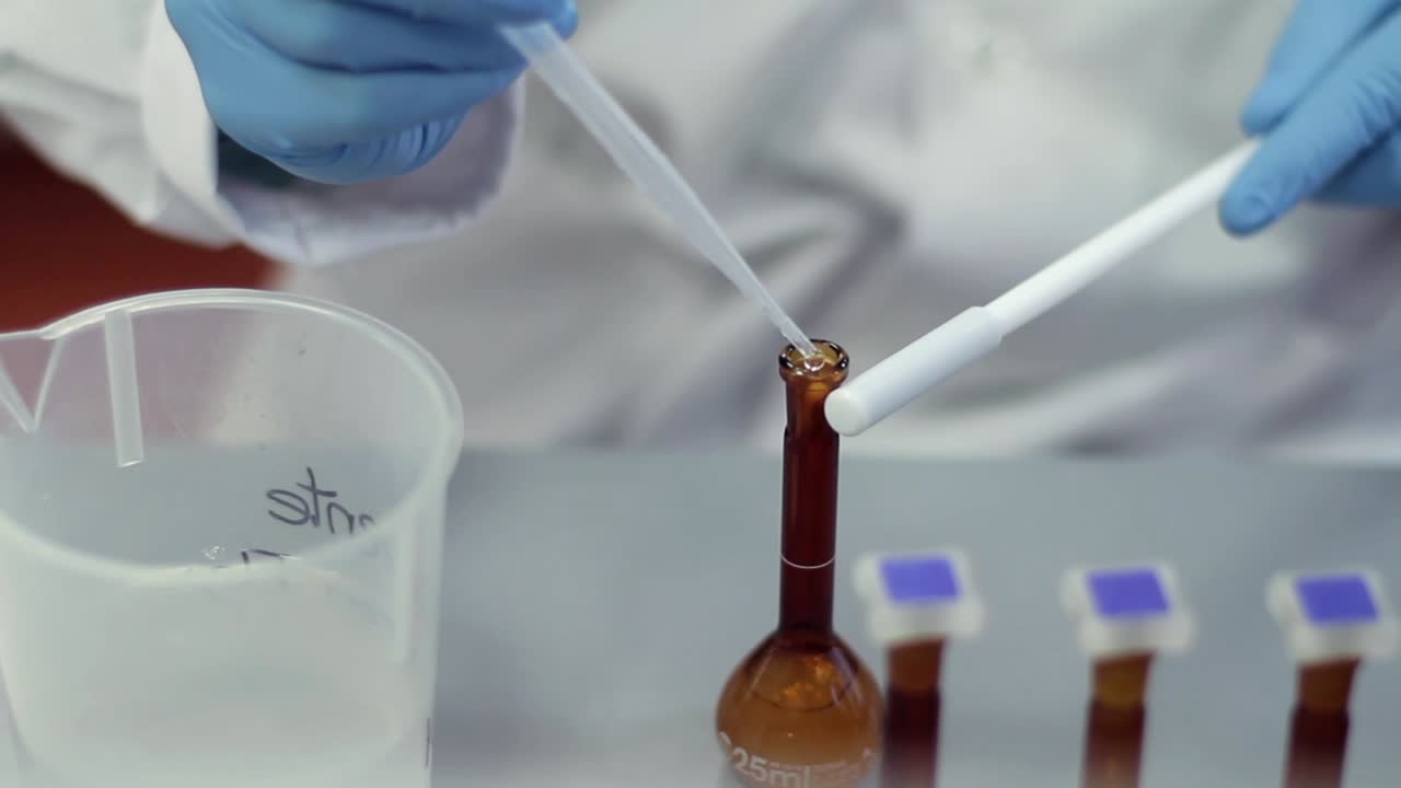 Scienziato con guanti da laboratorio che pipetta liquido in un pallone tarato.