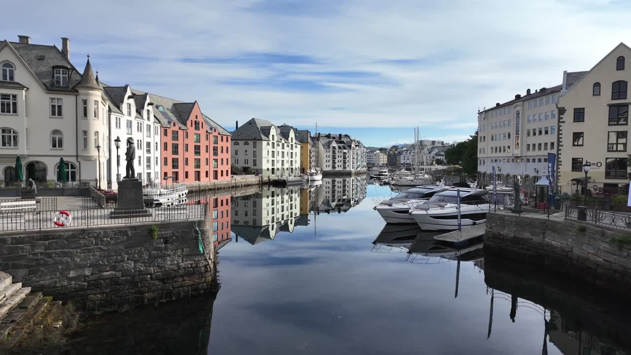 Scenografico canale sul lungomare ad Ålesund, Norvegia, con colorata architettura Art Nouveau che si riflette sull'acqua calma con barche ormeggiate sotto un cielo blu