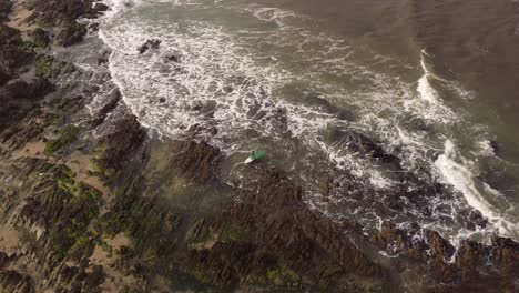 Aerial-shot-of-Surfer-with-Surfboard-entering-Atlantic-Ocean-for-surfing-during-large-waves---Walking-between-rocks-and-stones-at-shoreline