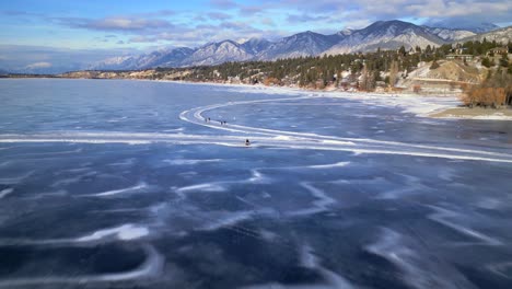 a drone passes over the heads of a couple sitting on a bench on top of the frozen surface of lake invermere, british columbia canada with skaters skating by