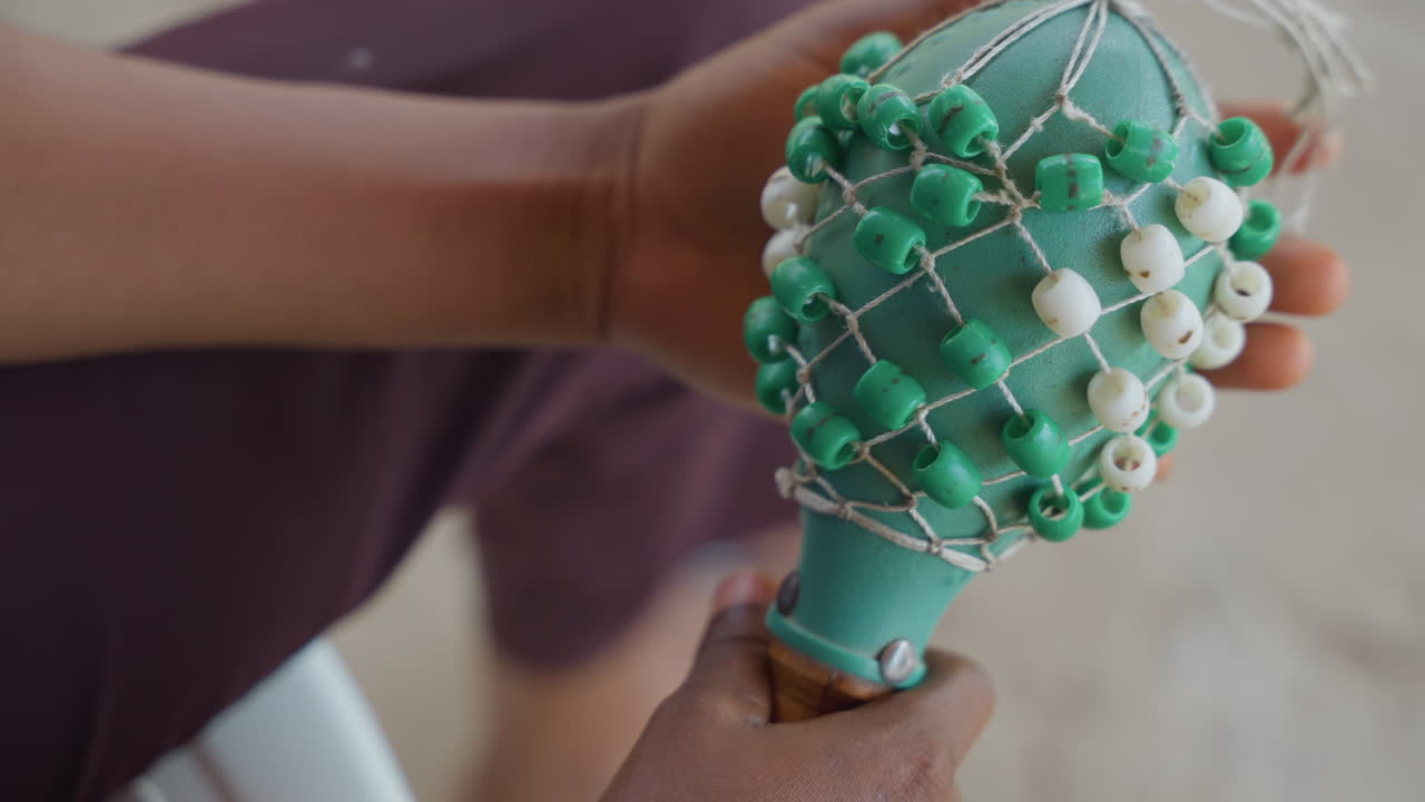 Maraca-Details prüfen. Hände untersuchen die Anordnung von Schnur und Perlen. Sorgfältige Prüfung der Maraca-Komponenten und der Handwerkskunst. Konzentrierte Hände analysieren und reparieren Maraca-Saiten und Zierperlen