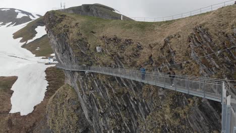 pedestrian suspension bridge over cliff with two people walking in the winter