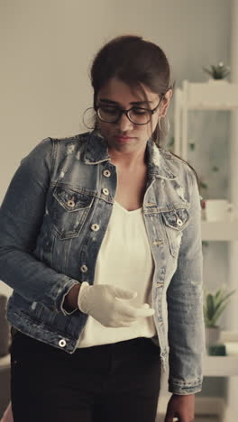 indian woman puts white rubber glove on hand to clean house. young housewife with glasses takes care of personal hygiene while doing routine chores