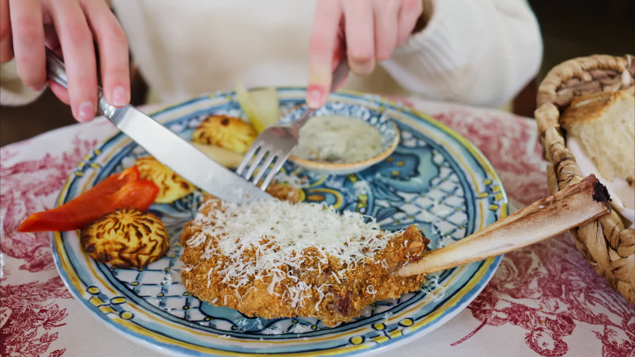 Close up of a woman cutting a piece of paneed meat and dipping it in sauce at a restaurant