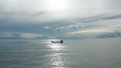 Helicopter-hovering-above-barge-to-load-goods-in-net-hanging-from-cable,-aerial