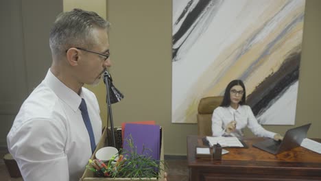 mature man leaving the office with a full box of supplies, walking in front of the secretary