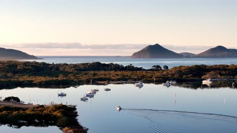 a-body-of-water-with-boats-floating-on-it-and-mountains-in-the-background-with-a-sky-background-and-a-few-clouds,-stunning-scene,-Australian-landscape