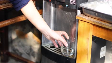 person fills glass with water from dispenser