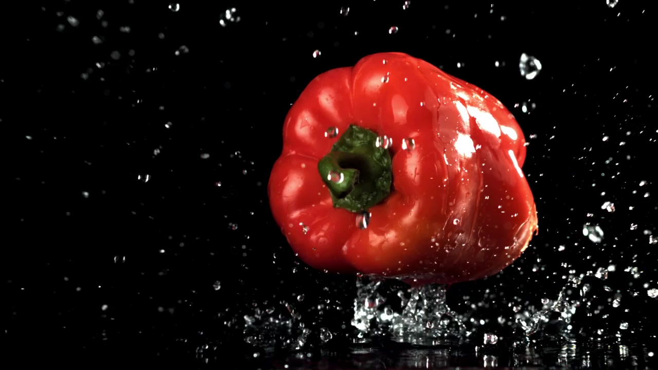 Čerstvá červená paprika dopadající do vody na černém pozadí