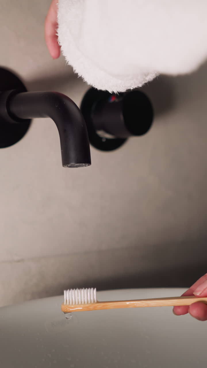 Lady washes toothbrush with water flow in bathroom closeup. Woman in terry bathrobe finishes dental care routine by cleaning toothbrush at home