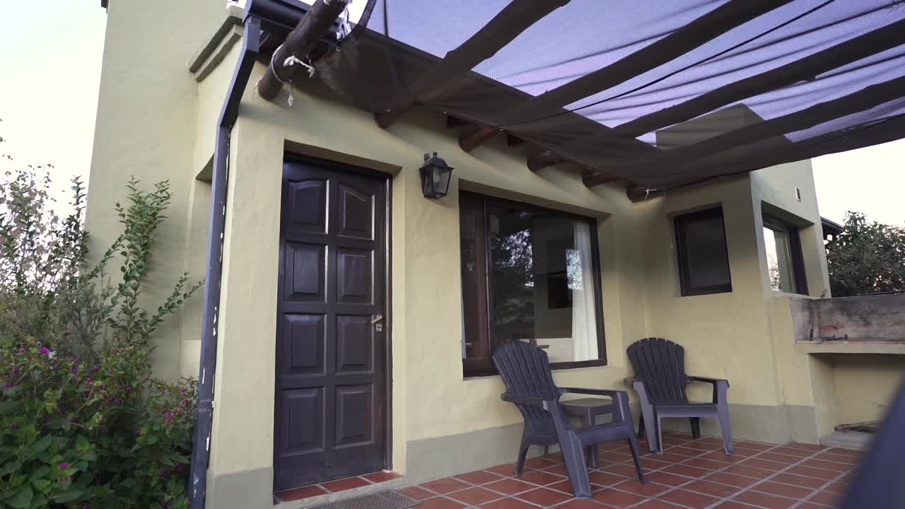 Establishing shot of cozy outdoor patio featuring two chairs under a sunshade, attached to a modern home with a black door and large windows
