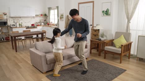 full length of cheerful asian family of three father, mother and daughter relaxing dancing to music in a modern bright home interior.