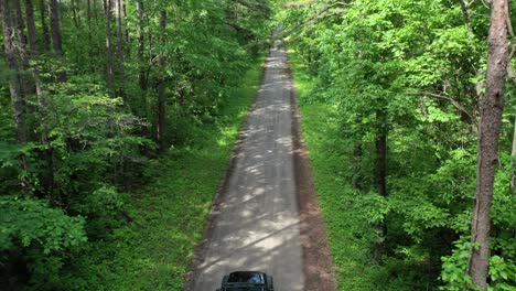 Vehicle-on-dirt-road-in-dense-green-forest-in-aerial-dangerous-fly