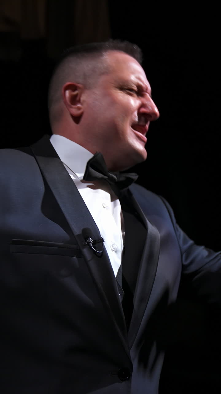 Actor in rich grey suit announces performance before auditorium. Theater curtains background. Dark background. Video from below. Vertical video