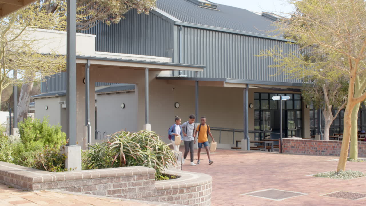 Multiracial students walking outside school, carrying backpacks and lunch bags, smiling together