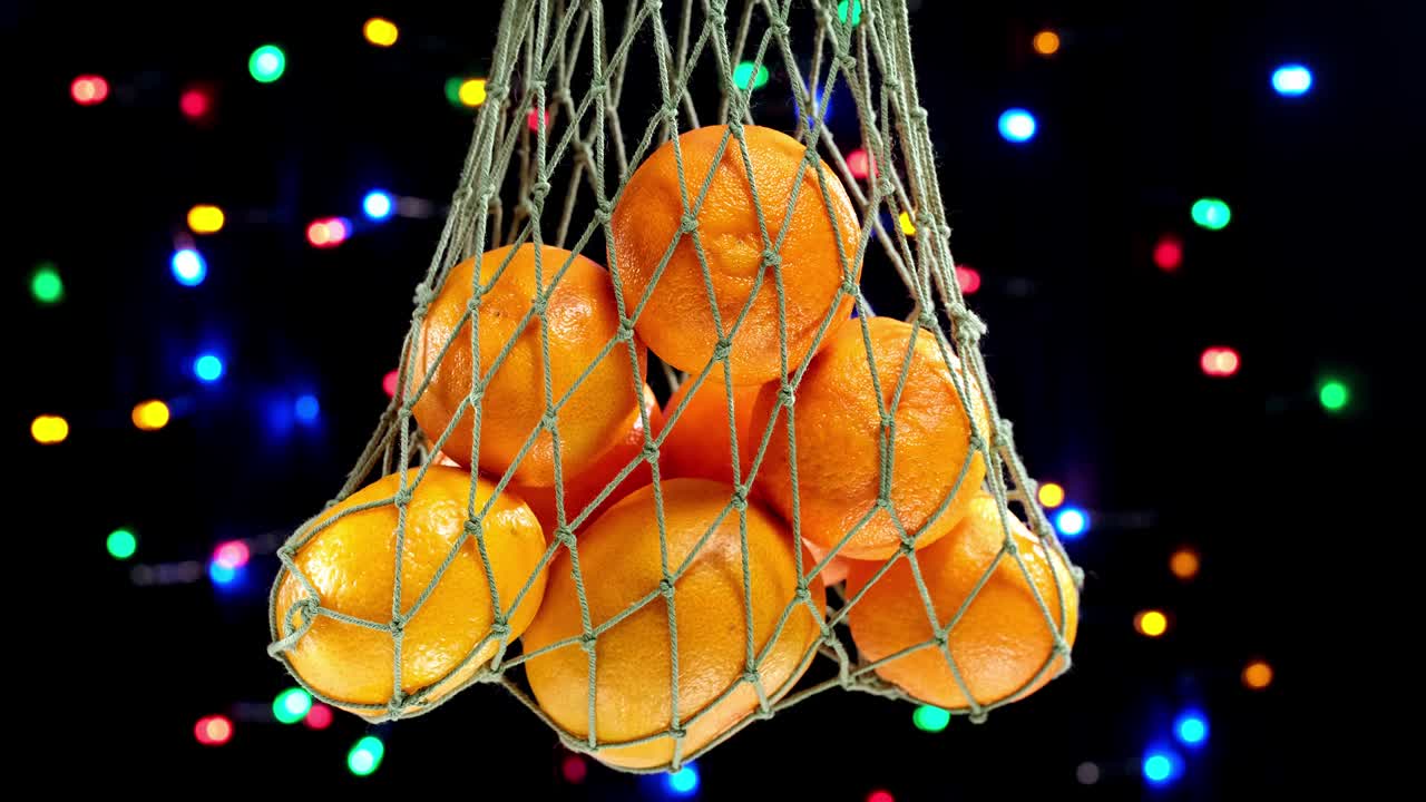 4k. bolsa de malla verde con frutas de mandarina naranja de navidad contra guirnaldas brillantes de navidad iluminadas en el fondo. guirnalda de año nuevo parpadeante.