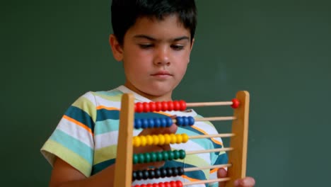 niño caucásico aprendiendo matemáticas con ábaco contra la pizarra verde en el aula 4k