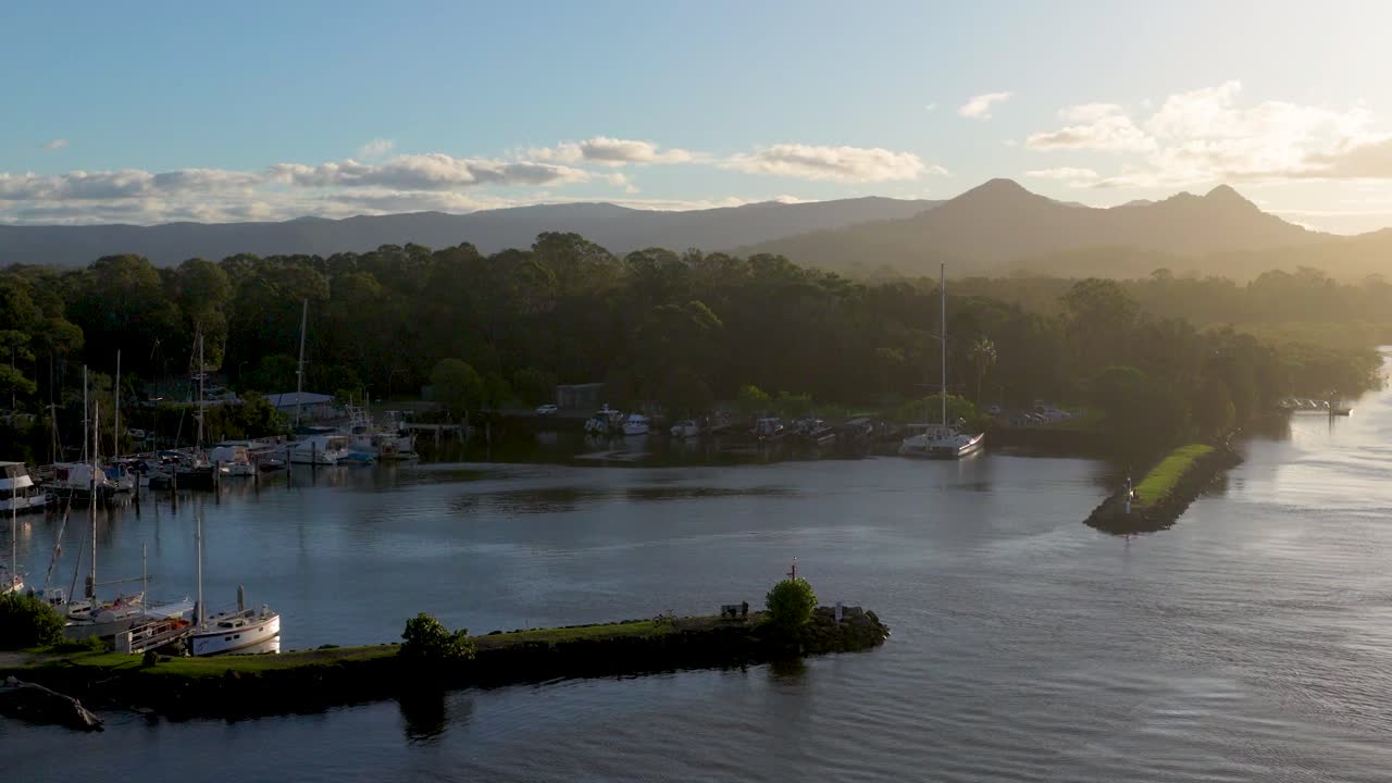 Aerial footage captures Brunswick Heads, Australia, with tranquil waters and lush greenery under warm sunset lighting