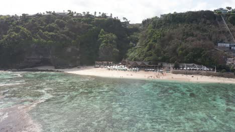 Fast-drone-forward-fly-over-Melasti-Beach-in-Bali-Indonesia-filming-peoples-kayaking-in-canoe