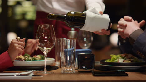 waiter pouring wine glass at fine restaurant table. couple enjoy fancy dining.