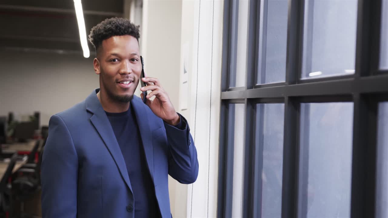 Happy african american male creative talking on smartphone at casual office, in slow motion