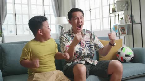 father and son celebrating a sports victory at home