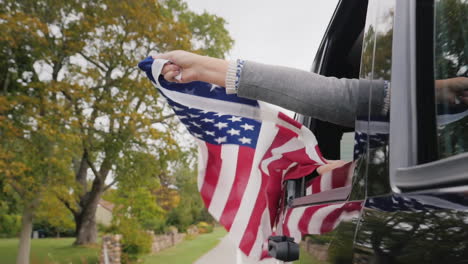 Hände-Halten-Amerikanische-Flagge-Aus-Dem-Autofenster