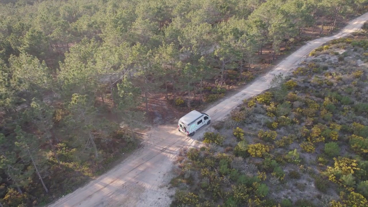 Campervan melaju di jalan berpasir yang dikelilingi hutan lebat di Nazare, Portugal.